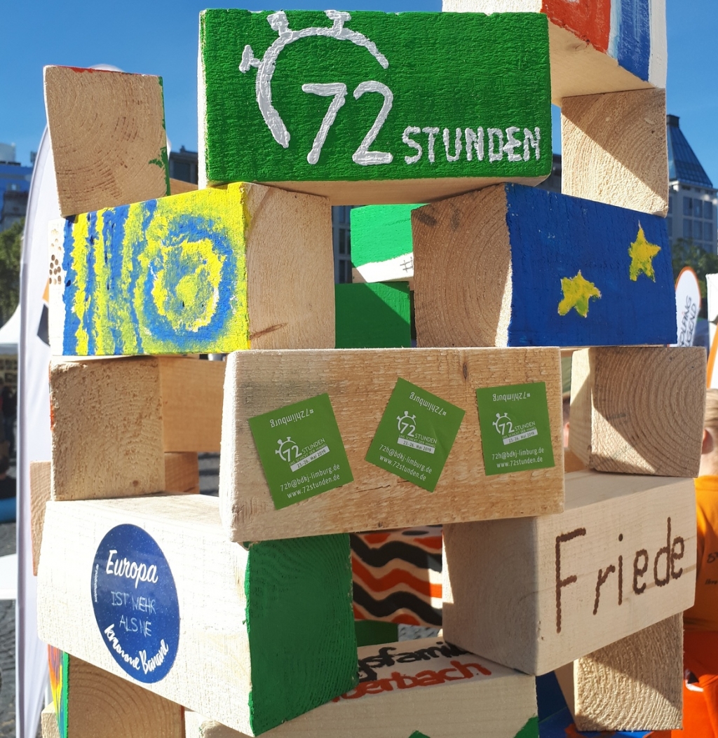 Gestapelte und bemalte Holzbalken, u.a. mit dem Logo der 72 Stunden Aktion. Foto BDKJ Bundesstelle Gestapelte und bemalte Holzbalken, u.a. mit dem Logo der 72 Stunden Aktion. Foto BDKJ Bundesstelle