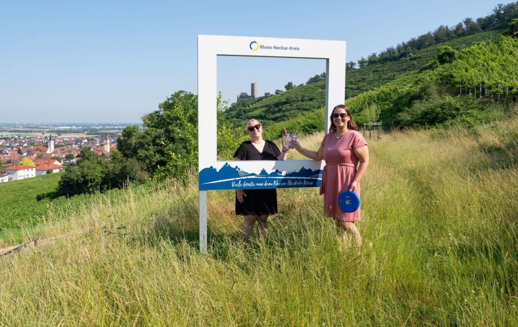 Bildunterschrift (Quelle: Landratsamt Rhein-Neckar-Kreis): Beim Fotowettbewerb „Sommer im Kreis“ sind der Kreativität keine Grenzen gesetzt – die einzige Bedingung: Das Foto muss mit einem der fünf Landschaftsfotorahmen aufgenommen werden. Hier ein Beispiel, zwei Frauen prosten sich durch den Rahmen zu, der auf einer Wiese steht. Bildunterschrift (Quelle: Landratsamt Rhein-Neckar-Kreis): Beim Fotowettbewerb „Sommer im Kreis“ sind der Kreativität keine Grenzen gesetzt – die einzige Bedingung: Das Foto muss mit einem der fünf Landschaftsfotorahmen aufgenommen werden. Hier ein Beispiel, zwei Frauen prosten sich durch den Rahmen zu, der auf einer Wiese steht.