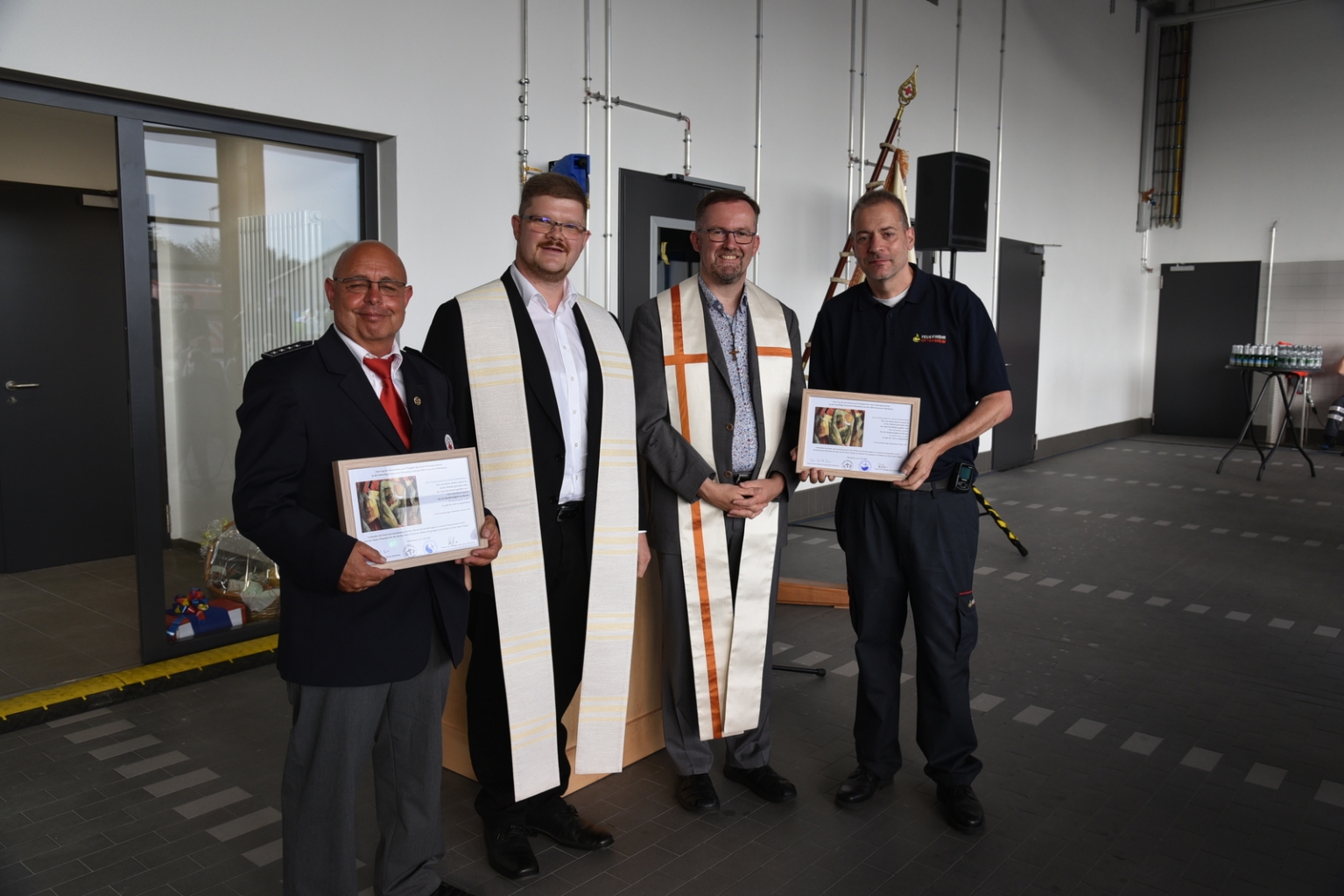 Der evangelische Pfarrer Tobias Habicht und sein katholischer Kollege Pfarrer Uwe Lüttinger übergeben gerahmte Segenswünsche an den DRK-Ortsvereinsvorsitzenden Hans-Thomas Dilger und den Feuerwehrkommandanten Rüdiger Laser.