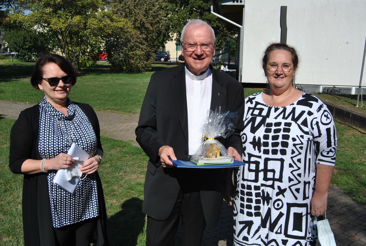 Marion Kolb und Carmen Kurz-Ketterer überreichen Pfarrer Wolfgang Gaber das Geschenk der kath. Kirchengemeinde.